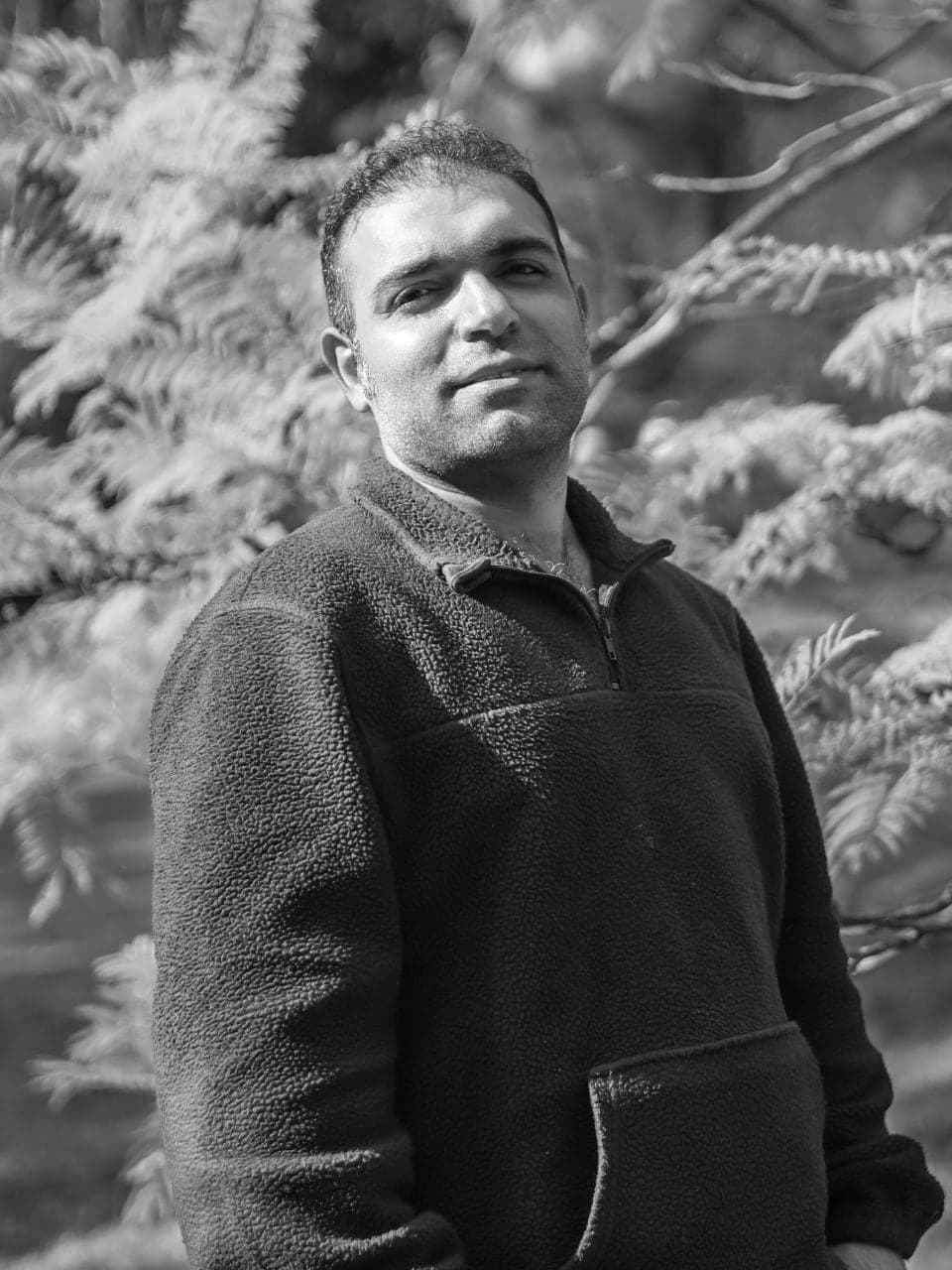 Amir standing among autumn trees, in black and white